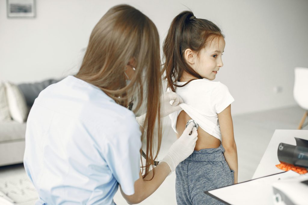 A female doctor uses a stethoscope to examine a child in a medical examination room.